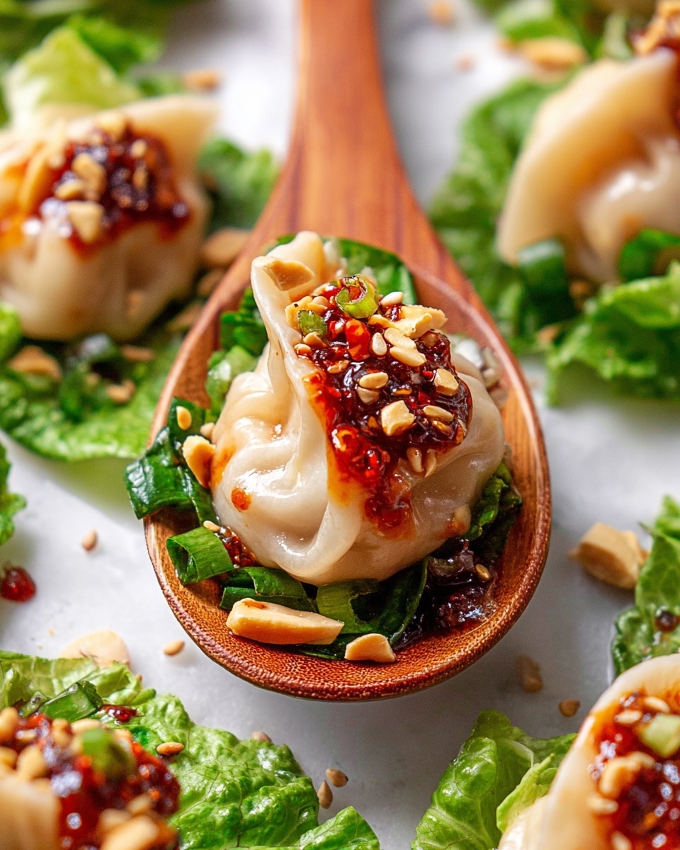 A white plate filled with a bed of fresh green lettuce leaves mixed with thin slices of purple onion and scattered peanuts, forming the base layer. On top, there are six plump, beige dumplings with smooth, slightly shiny surfaces, each topped with a bright red chili oil sauce that has small bits of chili flakes. The dumplings are garnished with sesame seeds and chopped green herbs, adding specks of white and green across the dish. The whole plate sits on a white marbled surface with a soft background that includes a red pepper. Photo taken with an iphone --ar 4:5 --v 7