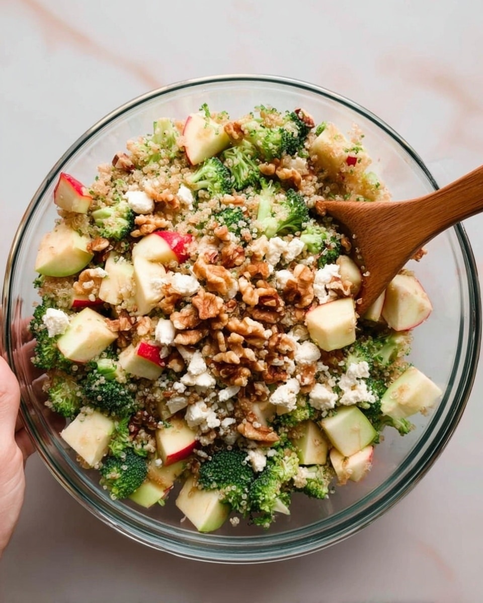 The image shows several small white bowls arranged on a white marbled surface, each bowl containing different ingredients around a larger white bowl filled with cooked quinoa. Surrounding the quinoa bowl are bowls with chopped broccoli, chopped nuts, crumbled feta cheese, mustard, lemon, honey, and olive oil. There is also a whole red apple and a wooden pepper grinder. The ingredients are fresh and colorful with a focus on green, beige, and yellow tones, all neatly placed for easy access. photo taken with an iphone --ar 4:5 --v 7