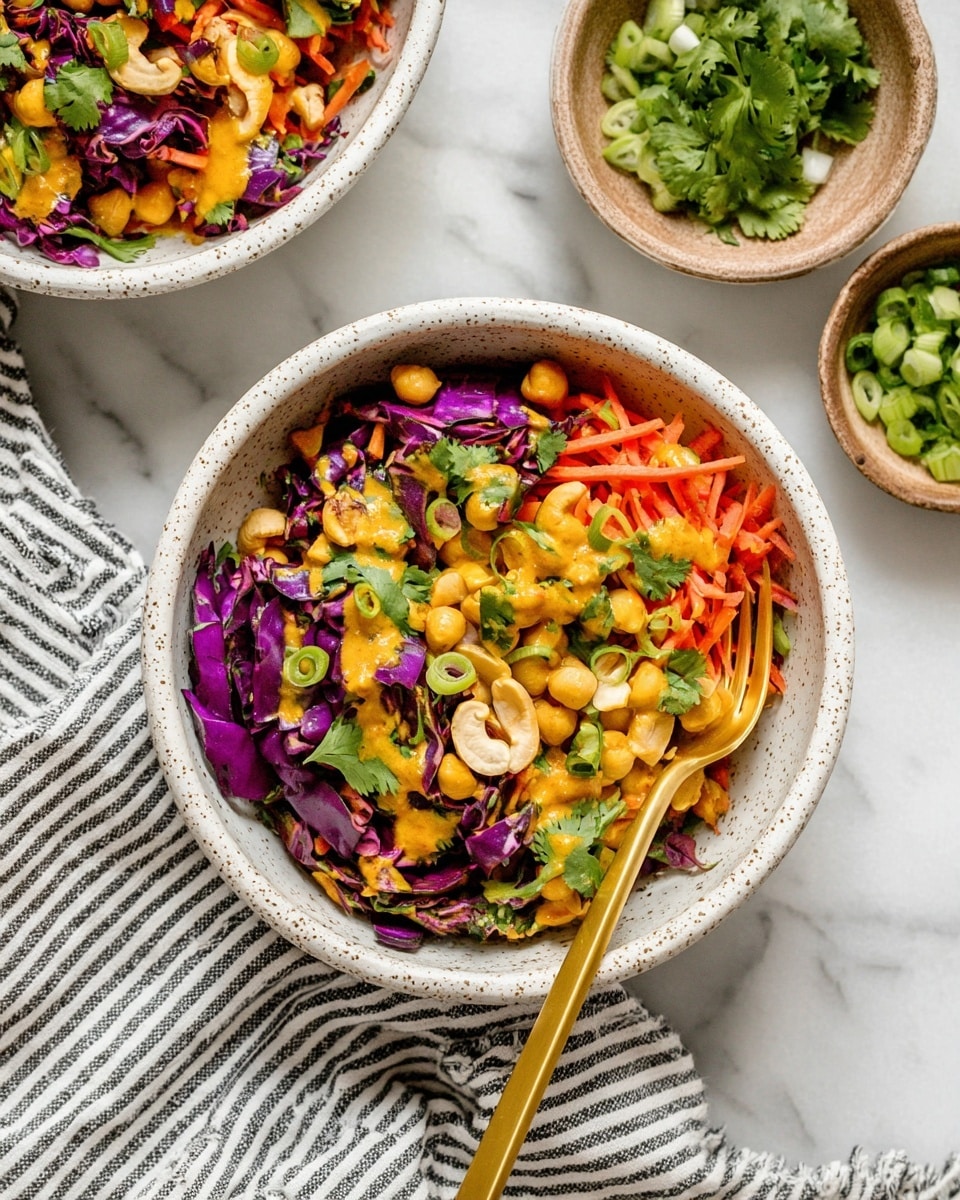 A white speckled bowl filled with a colorful salad showing three main layers: at the bottom, deep purple cabbage leaves with a crinkled texture; in the middle, bright orange shredded carrots mixed with golden chickpeas and creamy cashew nuts; on top, scattered green cilantro leaves and rings of fresh light green scallions, all drizzled lightly with a vivid orange dressing. A gold spoon rests inside the bowl on the right side. In the background, parts of two similar bowls and a small bowl of chopped cilantro sit on a white marbled surface, with a black and white striped cloth beneath the main bowl. Photo taken with an iphone --ar 4:5 --v 7