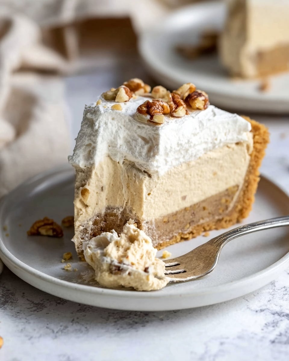 A round pie with a thick crumbly crust that is light brown and holds the filling well. Inside, there are three visible layers: the bottom layer is crunchy with bits of nuts mixed in, the middle layer is a smooth creamy beige, and the top layer is a thick, fluffy white whipped cream spread unevenly with whole and chopped pecans scattered over it. A slice is cut out, showing the clear division of the layers, and the pie rests on a round wooden board with a soft white cloth underneath. In the background, part of a white plate with the removed slice and a spoon is visible on a white marbled surface. Photo taken with an iphone --ar 4:5 --v 7