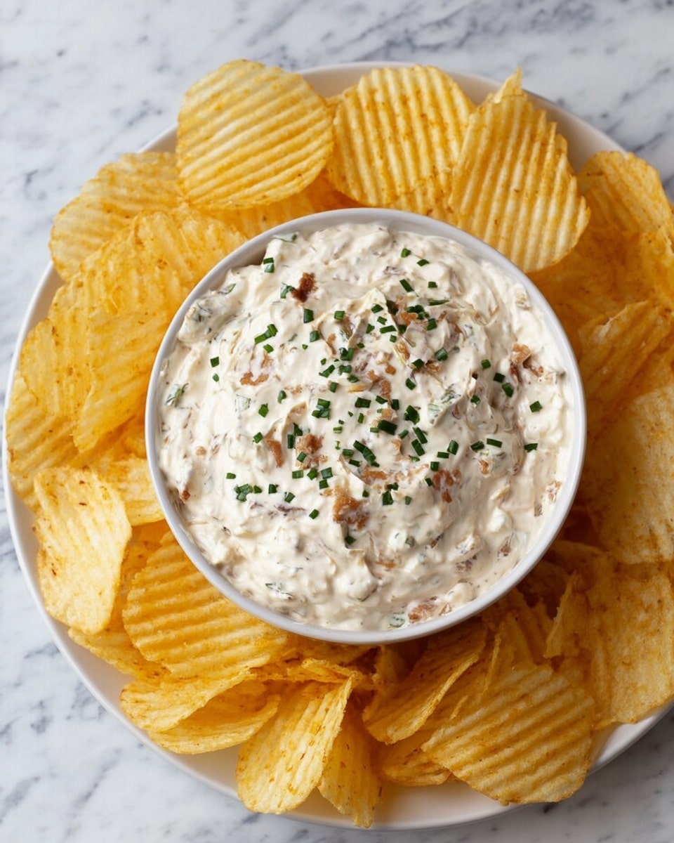 A white bowl filled with creamy, thick dip that has small brown bits mixed in, topped with scattered bright green chopped herbs. The bowl sits on a white plate that holds many ridged, golden-yellow potato chips arranged around the bowl. A woman's hand with red painted nails is holding one chip dipped halfway into the smooth, textured dip. The background is a white marbled surface. photo taken with an iphone --ar 4:5 --v 7