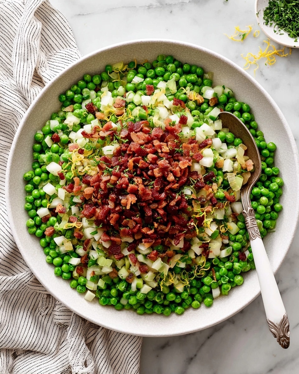 A large white bowl filled with a pea salad that has three main layers: the bottom layer shows bright green peas mixed with small cubes of pale white vegetables and thin slices of translucent onion, all evenly spread out; the top layer is a generous pile of small, browned, crispy diced bacon pieces placed right in the center; scattered throughout are bits of fresh green herbs and tiny yellow lemon zest curls adding a splash of color; the bowl sits on a white marbled surface next to a striped white and gray cloth, with a silver spoon featuring a white handle resting inside the bowl near the right edge. photo taken with an iphone --ar 4:5 --v 7