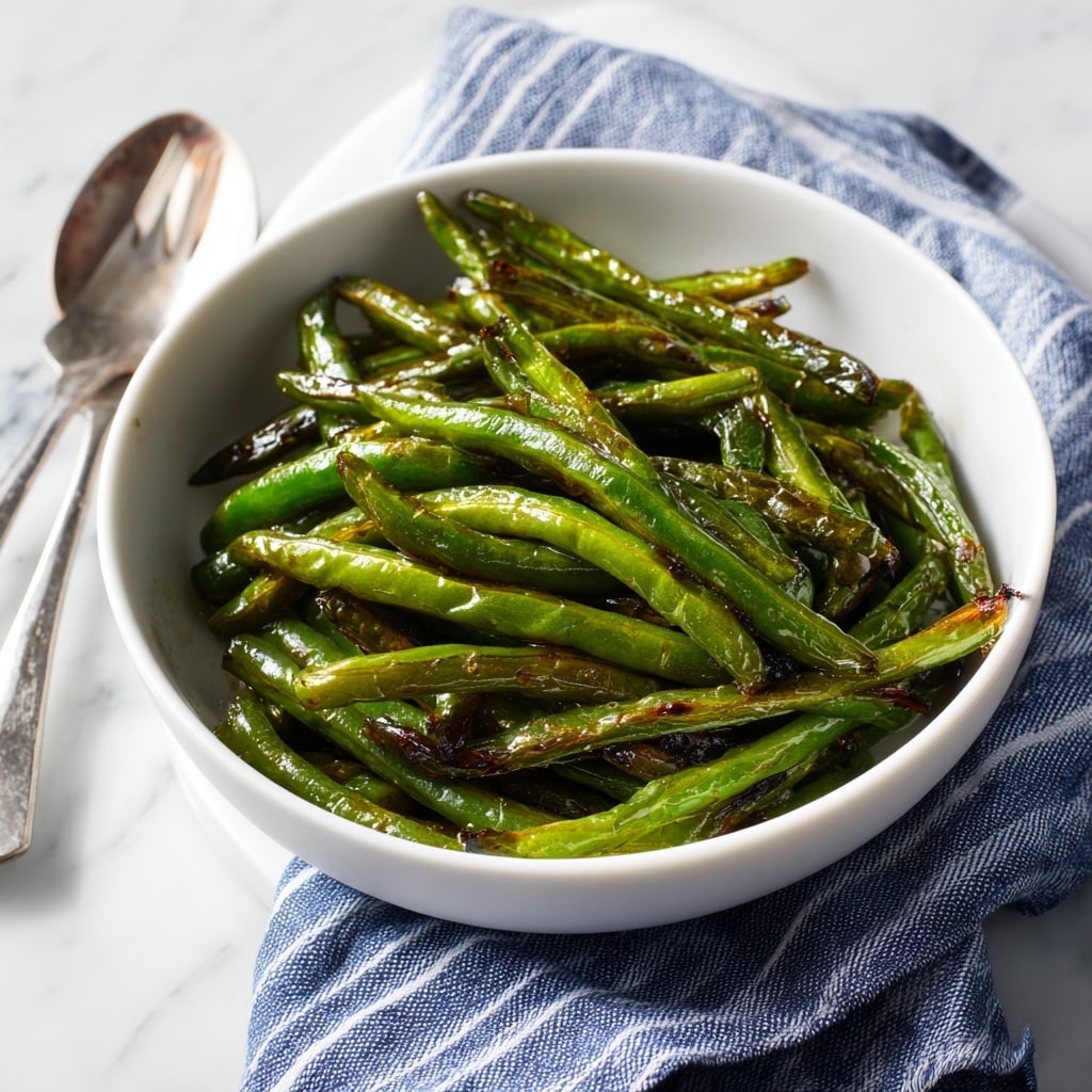 A white bowl holds a serving of cooked green beans, about two layers thick, with a shiny, slightly wrinkled texture and darkened spots showing they are roasted or sautéed; on top, there is one layer of crumbled reddish-brown bacon pieces scattered unevenly, adding a rich contrast to the green beans. The bowl sits on a white marbled surface with a vintage spoon partially under the bowl on the left, and a white plate with a silver fork on the right side. A blue and white striped cloth is softly draped under and around the bowl. Photo taken with an iphone --ar 4:5 --v 7