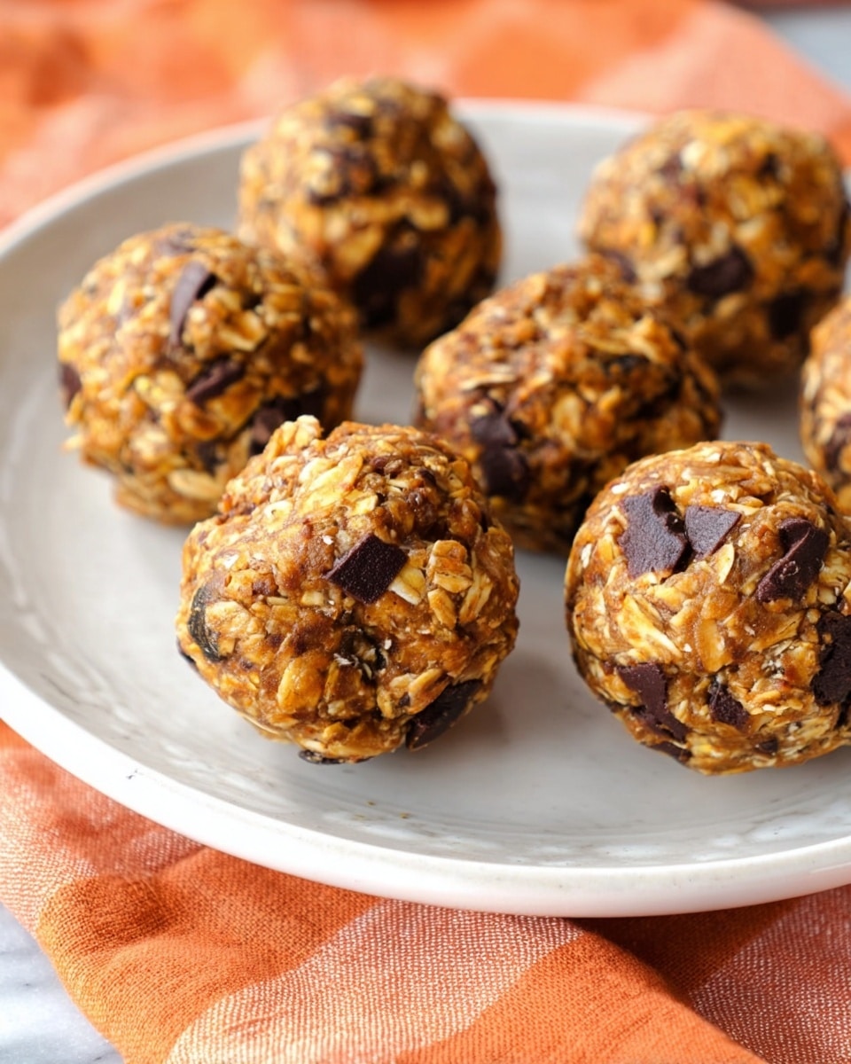 The image shows a white rectangular plate filled with small round balls made from oats, chocolate chunks, and a brown mixture that holds them together. Each ball is textured with visible oats and bits of dark chocolate scattered throughout, giving them a slightly rough look. The balls are arranged in neat rows on the plate, which has a delicate floral pattern along its edge. The plate sits on a dark surface, with an orange cloth featuring a white grid pattern partially visible in the corner, all placed on a white marbled background. photo taken with an iphone --ar 4:5 --v 7