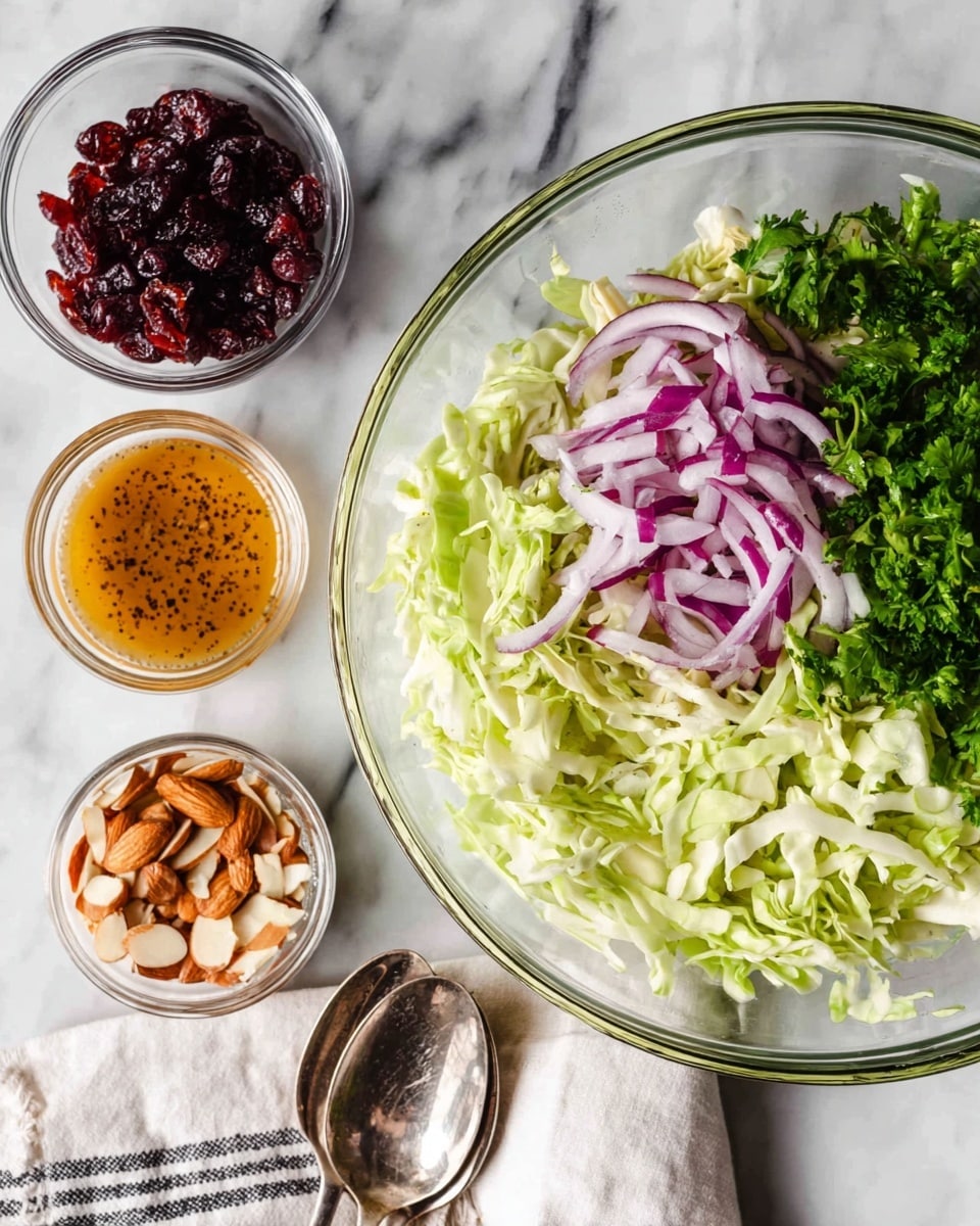 The image shows a white plate with a simple salad made of thin, shredded green cabbage and dark green leafy herbs layered on top. Scattered across the salad are small pieces of bright red dried cranberries and light brown sliced nuts. A few thin slices of purple onion are mixed in, adding color. A woman's hand holds a silver fork lifting a small mix of cabbage, herbs, onion, and cranberry from the plate. The plate rests on a rust-colored cloth, which sits on a wooden table, and in the blurred background, there is a wooden bowl filled with more salad. The photo is taken with an iphone --ar 4:5 --v 7