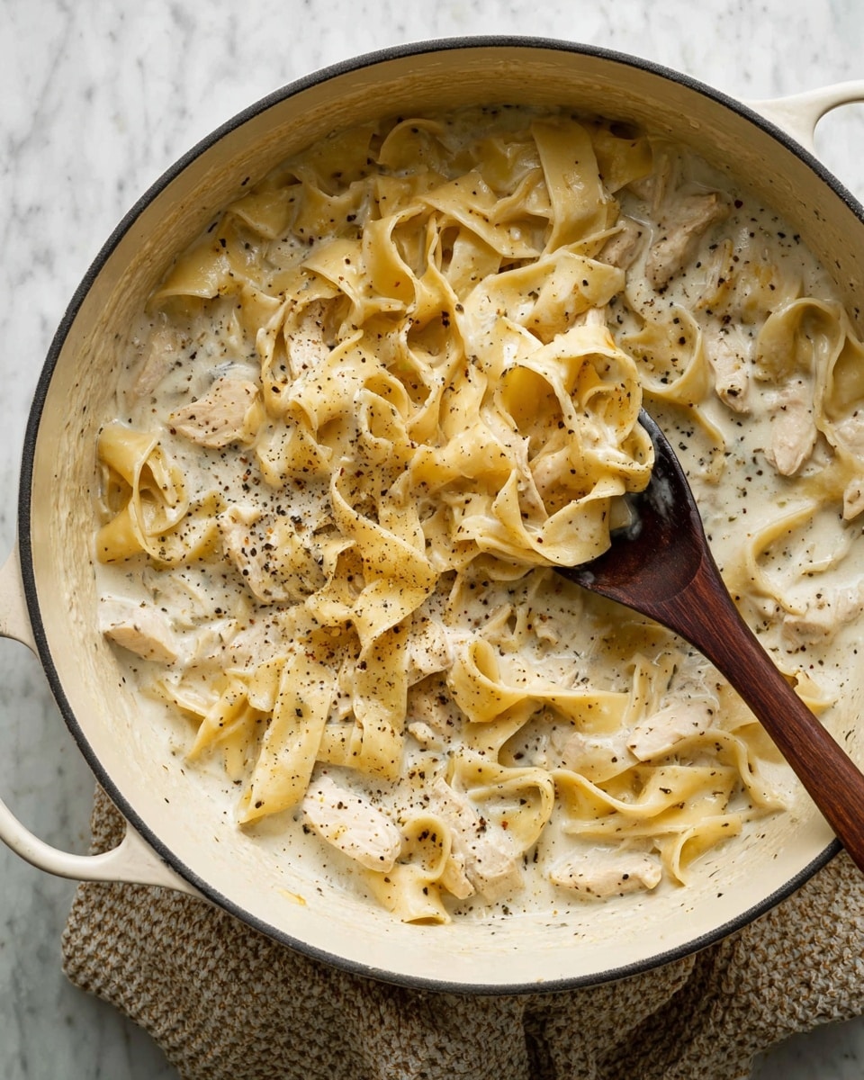 A bowl filled with a creamy white soup containing several layers of small pasta shapes and chunks of white meat, all coated in a thick, pale cream sauce with visible flecks of black pepper and herbs scattered through both the sauce and on top. The white bowl sits on a cloth with soft beige and gray stripes, placed on a white marbled surface. Near the bowl, a woman's hand holds a gold spoon gently dipped into the soup. Pieces of torn bread are visible on the upper edge of the image, adding a warm contrast to the creamy dish. Photo taken with an iphone --ar 4:5 --v 7