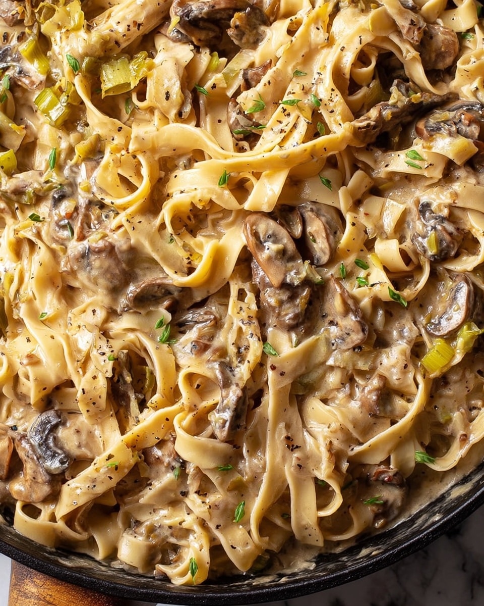 A white round bowl filled with creamy fettuccine pasta mixed with mushrooms. The pasta is light brown, creamy and soft, with thick flat noodles swirled around each other in about two layers. Dark brown, grilled or sautéed mushroom slices are mixed thoroughly throughout the pasta, some layered on top. Small light brown pine nuts are scattered on top along with a sprinkling of white grated cheese. The bowl is placed on a wooden surface with a white marbled texture, with some sage leaves and a small cup of pine nuts visible in the background. photo taken with an iphone --ar 4:5 --v 7