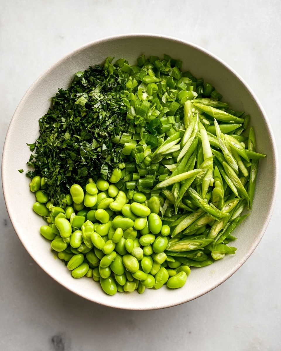 A white bowl holds a fresh mix of green vegetables in neat sections. At the bottom right are bright green edamame beans, smooth and round. Above and next to the beans are thin, diagonal slices of vibrant green snap peas, showing their seeds inside. On the top right side are more snap peas cut at an angle, adding a fresh texture. The left side of the bowl has finely chopped dark green herbs, creating a fine leafy layer. The bowl sits on a white marbled surface with a few scattered green pieces around it. photo taken with an iphone --ar 4:5 --v 7