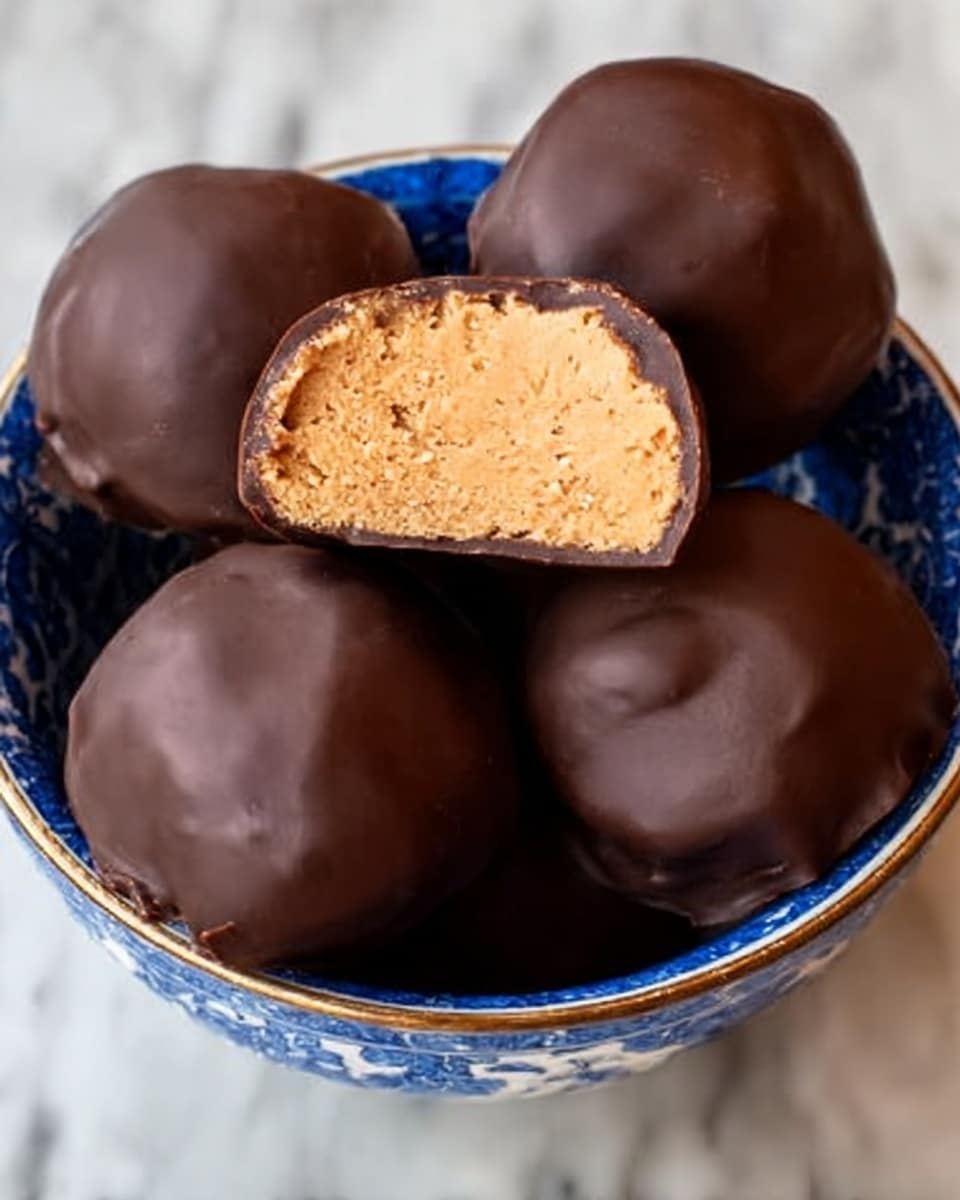 The image shows several round chocolate-covered peanut butter balls arranged on a reflective surface with a white marbled texture in the background. The peanut butter balls have two visible layers: the outer, smooth dark chocolate coating, and the inner, creamy light tan peanut butter filling that looks dense and slightly textured. Two of the peanut butter balls are cut in half and stacked in the center, clearly showing the thick peanut butter layer inside and the thin chocolate shell on the outside. The overall look is rich and inviting, with a focus on the smoothness of the chocolate and the creamy inner filling. Photo taken with an iphone --ar 4:5 --v 7