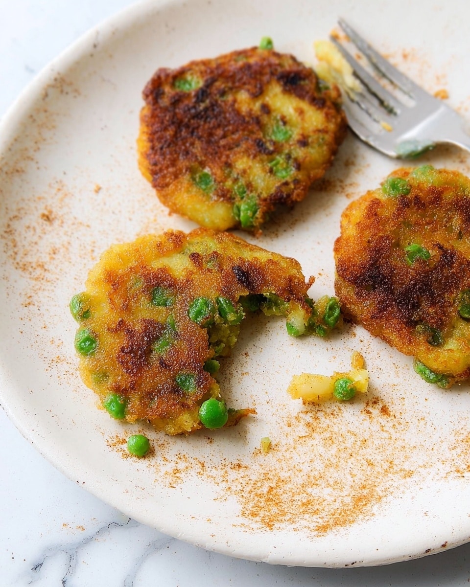 A stack of five thick, golden-brown fritters sits on a white plate, each fritter showing a crispy texture with scattered bright green peas and small bits of vegetables embedded within the soft, yellow dough. The top fritter has a slightly rough and crunchy surface with darker browned spots, while the edges of each fritter show a mixture of crispiness and softness. The white plate is placed on a blue cloth with a subtle chevron pattern, and the background is a soft turquoise color with a smooth, out-of-focus look. A silver fork lies next to the plate on the cloth. photo taken with an iphone --ar 4:5 --v 7