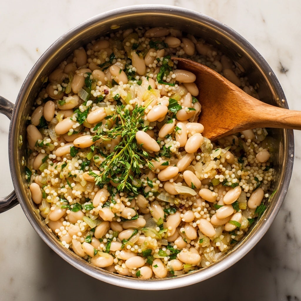 A close-up top view of a silver pot filled with cooked white beans, multi-colored small lentils in orange, green, and beige, and translucent chunks of cooked onion, all mixed together. Visible fresh green herb sprigs rest on top, adding a touch of green. A wooden spoon with a warm light-brown handle is stirring the mixture on the right side. The pot is placed on a stove with a white marbled texture background visible around the edges. photo taken with an iphone --ar 4:5 --v 7