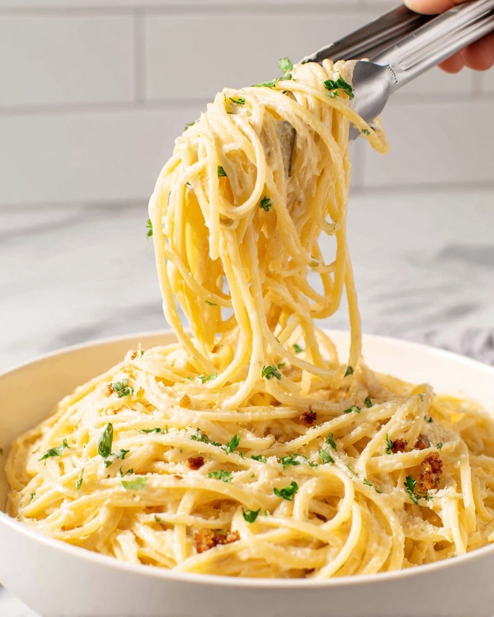 A close-up top view of a large white plate filled with creamy spaghetti pasta in a smooth, pale yellow sauce, topped with small golden-brown crispy cubes scattered all over and finely chopped green herbs sprinkled over, with a few fresh green basil leaves placed on top for color. The spaghetti is twirled in layered swirls across the plate. Around the plate, there is a small white bowl filled with grated cheese, two whole white garlic bulbs, a small white dish with chopped green herbs, and some green basil leaves on a white marbled surface. Three golden forks and a golden fork rest are positioned near the plate, and a pair of golden chopsticks rests partly on the plate. photo taken with an iphone --ar 4:5 --v 7