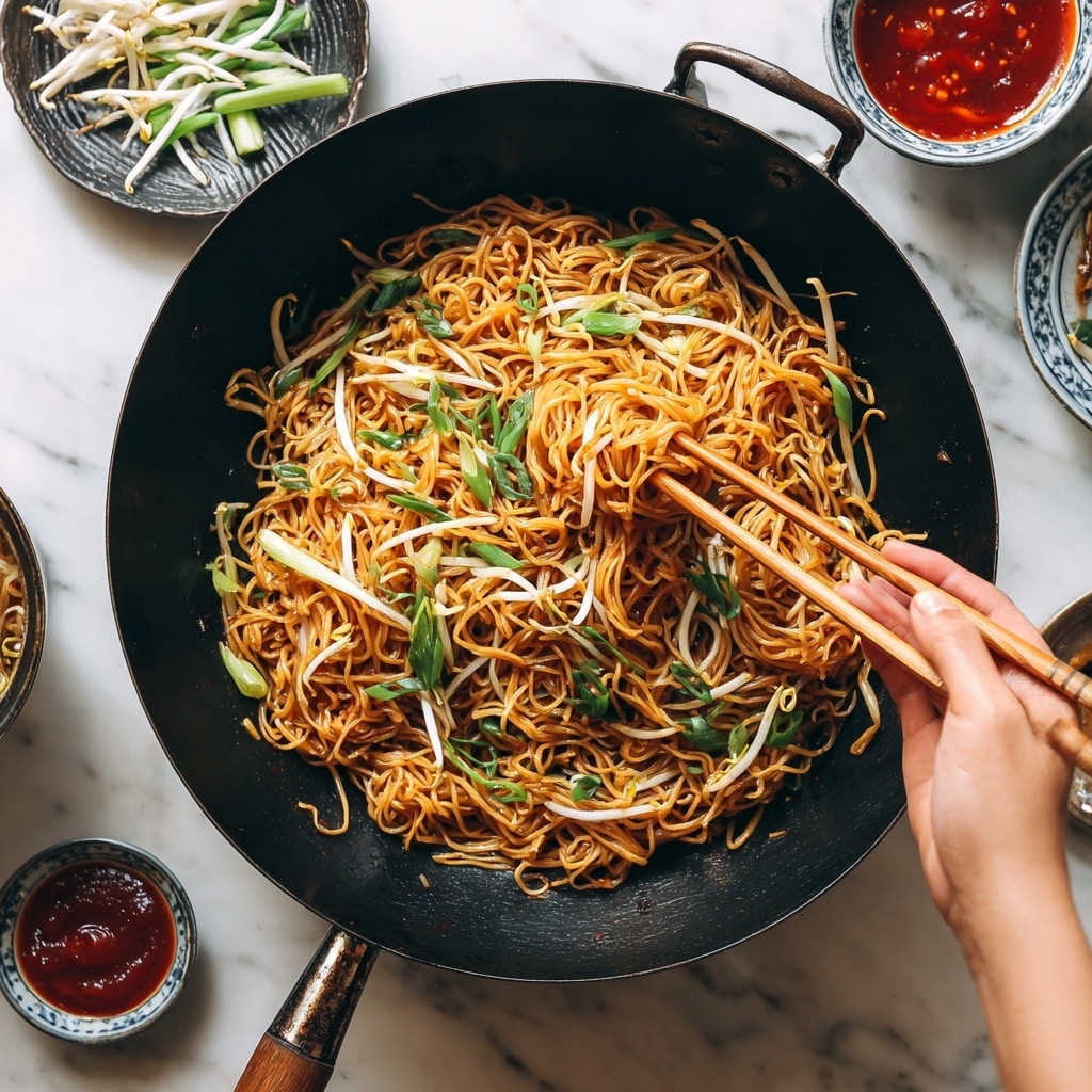 A round black plate holds a heap of thin cooked noodles, golden brown with a slightly shiny texture, mixed with light green scallions and white bean sprouts scattered throughout. Long, slender dark brown chopsticks rest on the right side of the plate. Nearby on the white marbled surface, a small white dish with a blue floral pattern sits above, and a beige bowl with a deep red sauce is at the top left corner. At the bottom right, a small textured white bowl contains sliced green scallions, with a few pieces scattered around it. The scene is set on a white marbled texture background with a dark cloth partially visible under the plate. Photo taken with an iphone --ar 4:5 --v 7