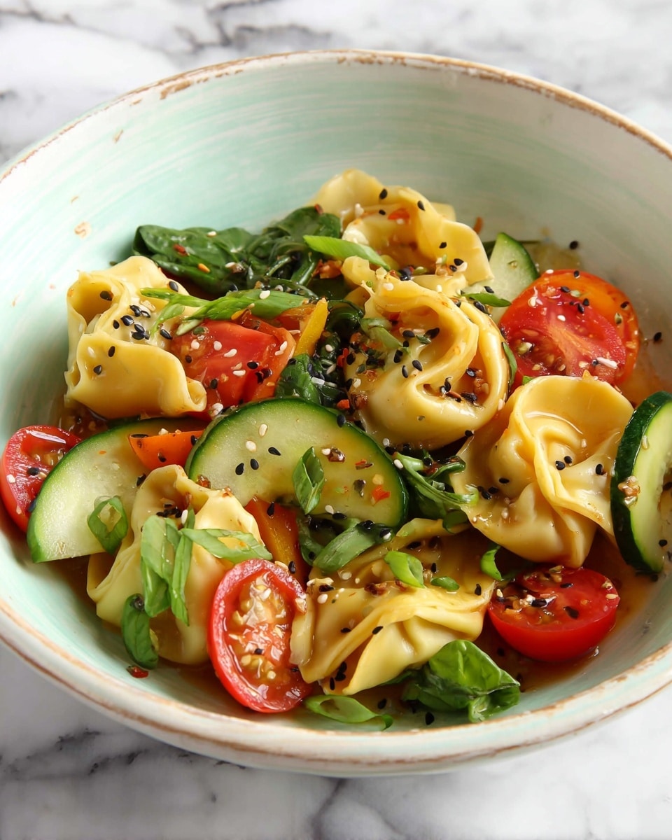 The dish shows several large, soft yellow tortellini pasta pieces mixed with fresh, sliced red and yellow cherry tomatoes and thin cucumber rounds. Bright green spinach leaves and chopped scallions add a fresh layer, all lightly coated in a glossy sauce with black sesame seeds sprinkled evenly on top. The food is served in a white bowl with a subtle rustic design, set against a white marbled surface. photo taken with an iphone --ar 4:5 --v 7