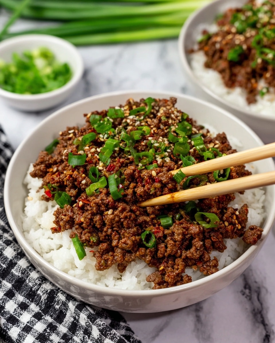 The image shows two white bowls filled with a two-layer dish. The bottom layer is white rice with a soft, fluffy texture, and the top layer is a generous amount of cooked ground beef that looks juicy and slightly crumbly with small bits of red pepper flakes mixed in. The beef is garnished with bright green chopped scallions and sprinkled with white sesame seeds. Two light wooden chopsticks are picking up some beef from the front bowl, which rests on a cloth with a black and white checkered pattern, all placed on a white marbled surface. In the background, there are fresh green scallions and a small white dish with extra chopped scallions visible. Photo taken with an iphone --ar 4:5 --v 7