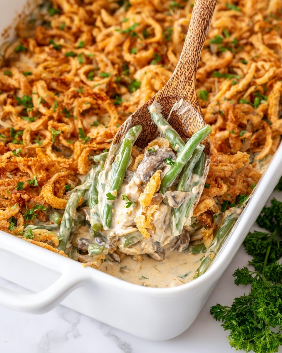The image shows a white rectangular casserole dish with three main layers visible. The bottom layer is made of green beans coated in a creamy, light beige sauce mixed with bits of mushrooms. The middle layer is thick and creamy, binding the green beans, mushrooms, and small pieces of onion together. The top layer has a generous amount of golden brown, crispy fried onion rings sprinkled with small green herb pieces. A wooden spoon is scooping out some of the creamy green bean mixture, revealing the layers underneath, all set on a white marbled surface with some green parsley placed nearby. Photo taken with an iphone --ar 4:5 --v 7
