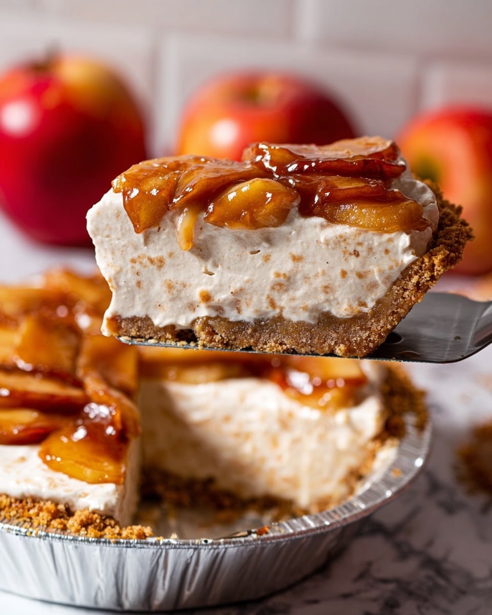 The image shows a slice of creamy pie being lifted above the rest of the pie. The pie has three layers: the bottom layer is a light brown crumbly crust, the middle layer is a thick and smooth off-white cream filling speckled with tiny bits, and the top layer consists of glossy, golden-brown caramelized fruit slices, likely apples, with a shiny glaze. The pie is in a silver pie tin, placed on a white marbled surface, with two red apples blurred in the background. A woman's hand is holding the pie slice with a flat spatula. Photo taken with an iphone --ar 4:5 --v 7