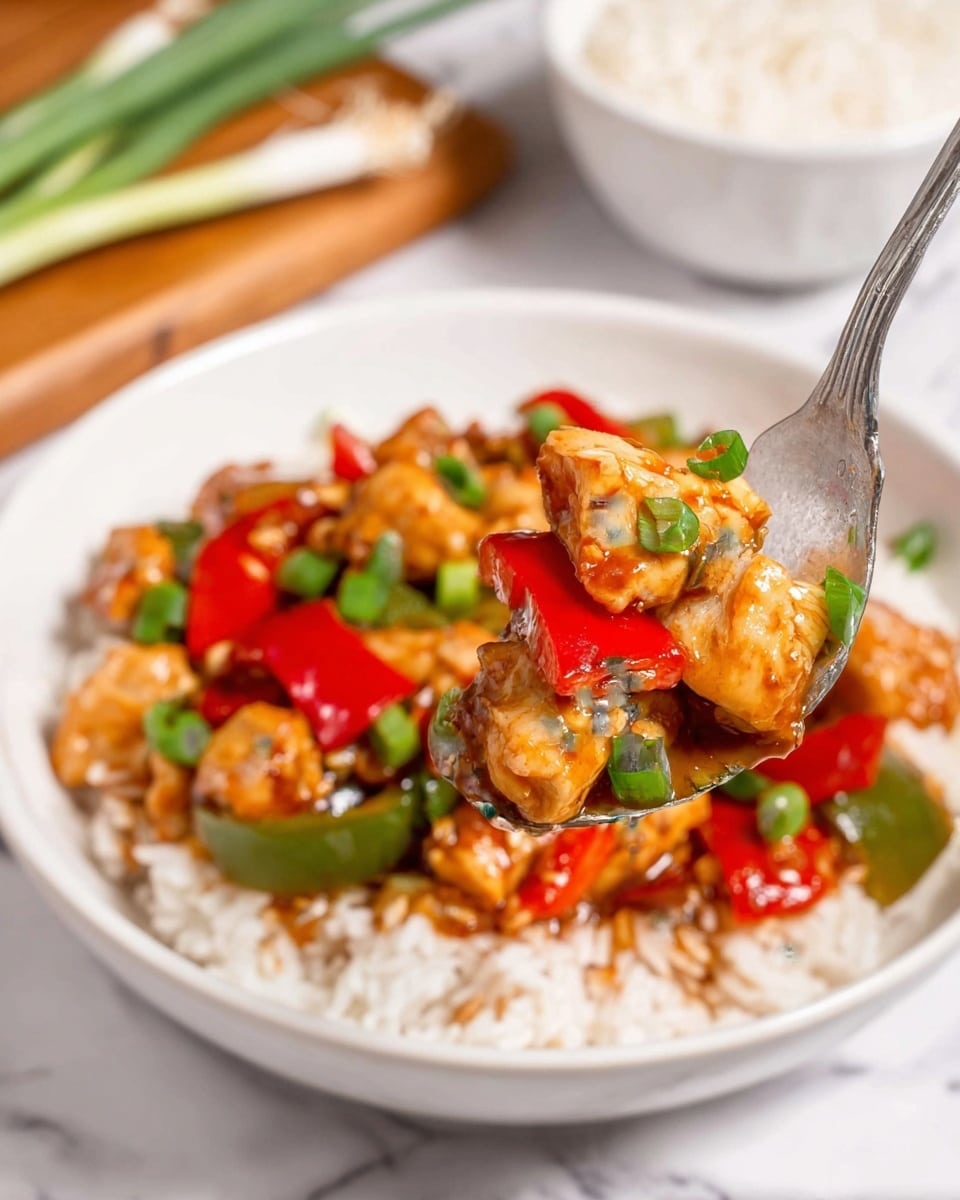 A black cast iron pan filled with three main layers: the bottom shows a glossy dark brown sauce, on top are chunky pieces of cooked orange-brown chicken, bright red and green bell pepper chunks, and several whole dried red chili peppers. Scattered on top are small chopped green onions and light brown peanuts, adding texture. The pan sits on a white marbled surface near a bowl of white rice and a wooden board with green onions and garlic visible, all beneath soft natural lighting. photo taken with an iphone --ar 4:5 --v 7