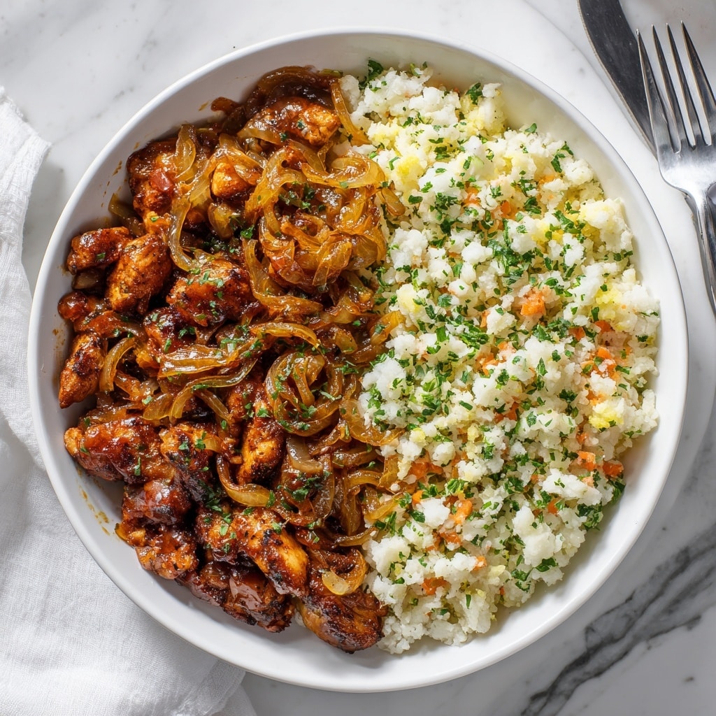 A round white bowl filled with two distinct layers: on the left side, a thick layer of brown stewed meat covered in glossy, soft, cooked onions with a rich sauce, showing tender texture and some green herb bits; on the right side, a separate layer of fluffy white cauliflower rice mixed with finely chopped carrot pieces and green herbs, giving a colorful contrast. The bowl sits on a white marbled surface, with part of a fork and a folded white cloth in the blurry background. Photo taken with an iphone --ar 4:5 --v 7