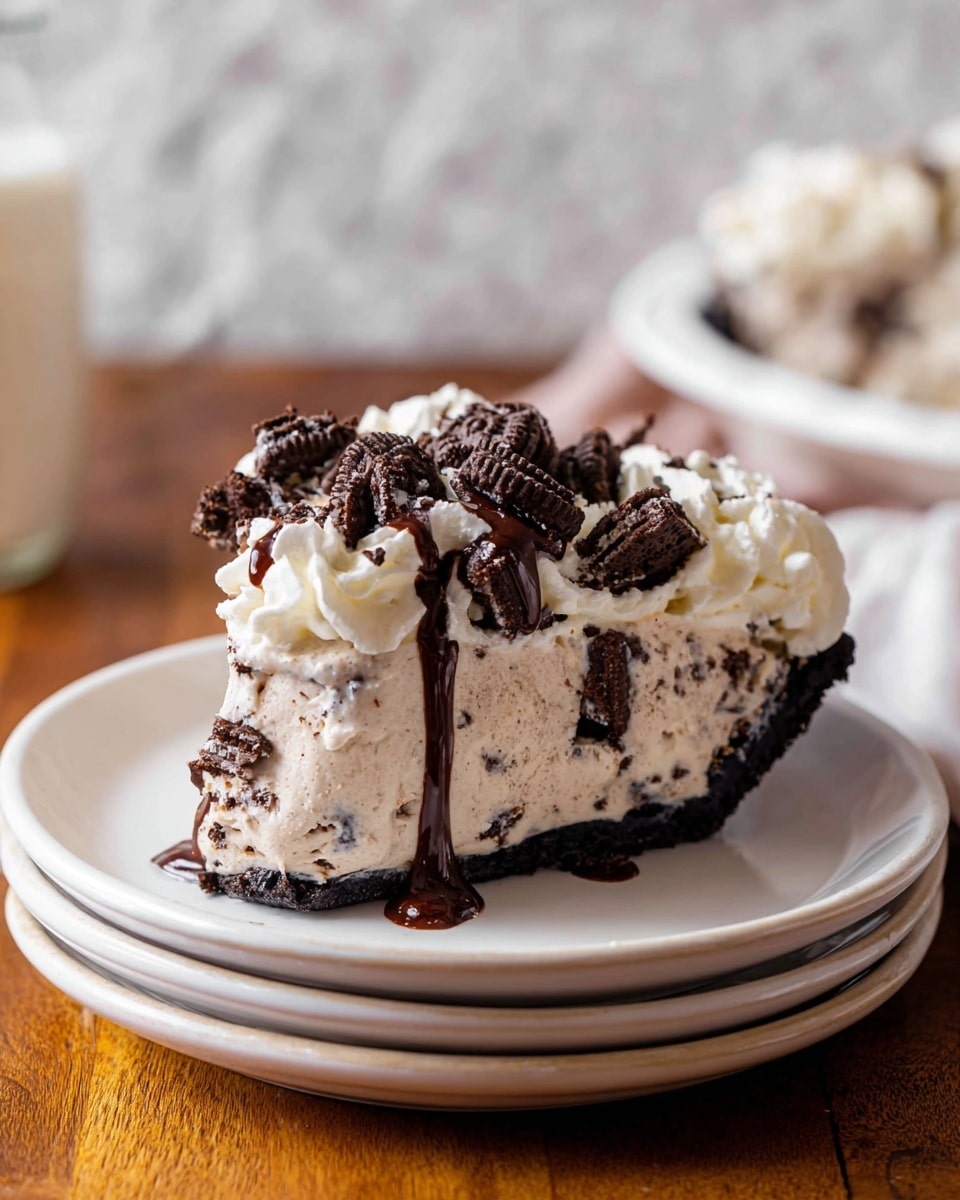 A slice of cookies and cream ice cream cake sits on a white plate. The cake has two layers: a dark chocolate cookie crumb crust at the bottom and a thick creamy white layer with specks of crushed cookies inside. It is topped with whipped cream, larger chunks of chocolate sandwich cookies, and a drizzle of rich dark chocolate syrup flowing over the sides. There are some cookie crumbs scattered around the plate. The background has a soft focus with a white marbled texture and kitchen items blurred out. photo taken with an iphone --ar 4:5 --v 7