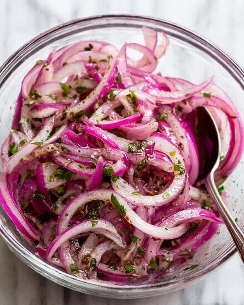 A clear glass bowl holds thinly sliced red onions, which have a light pink to purple color with translucent edges. The onions are mixed with small green herb pieces, likely parsley, adding specks of bright green throughout. The mixture appears lightly coated with a shiny dressing and is sprinkled with small black pepper flakes that add texture. A spoon with a turquoise handle and gold scoop rests inside the bowl, partially submerged in the onion salad. The bowl sits on a white marbled surface. Photo taken with an iphone --ar 4:5 --v 7