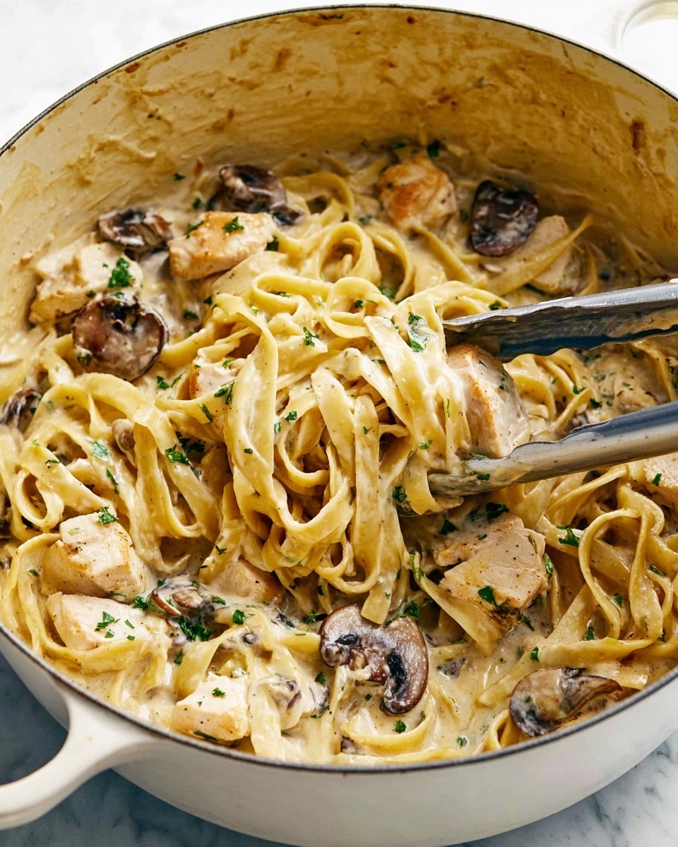 A close-up view of creamy pasta in a white pot, showing three main layers: the bottom layer is coated fettuccine noodles in a smooth beige cream sauce, the middle layer features chunks of white chicken pieces and dark brown sliced mushrooms evenly mixed throughout, and the top layer has small bits of chopped green herbs sprinkled for color contrast, with metal tongs partially visible holding some pasta and a chicken piece, all set against a soft white marbled surface. photo taken with an iphone --ar 4:5 --v 7