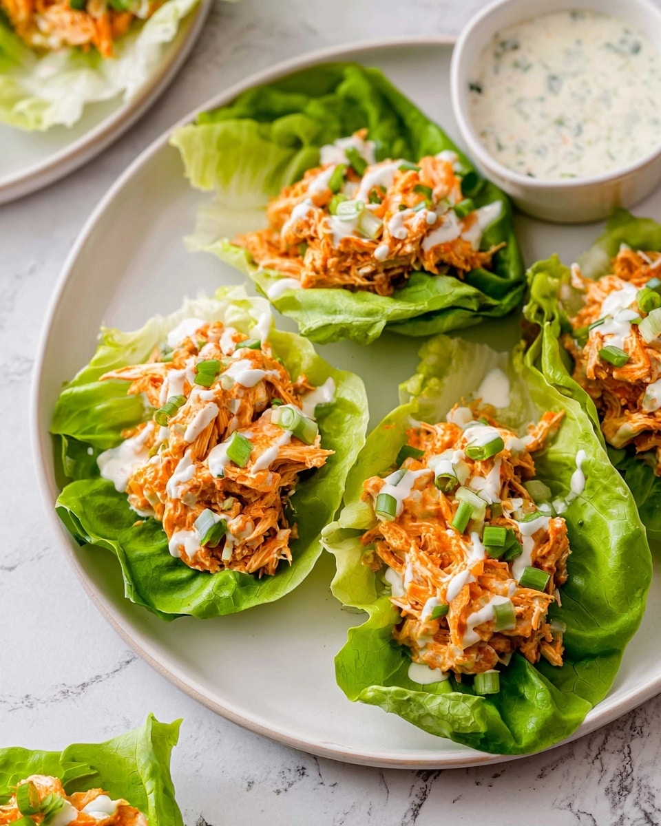 The image shows a white plate with five bright green lettuce leaves placed flat, each holding a small pile of shredded chicken mixed with orange sauce and small bits of celery. The chicken mixture is topped with a drizzle of creamy white dressing and sprinkled with chopped green onions. The plate sits on a white marbled surface, with a small white bowl of dressing placed nearby. The colors are fresh and vibrant, with a mix of green, orange, and white in a simple, clean presentation. photo taken with an iphone --ar 4:5 --v 7